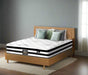 Bed with pillows and a mattress on a wooden bed frame against a green wall with a plant and artwork.